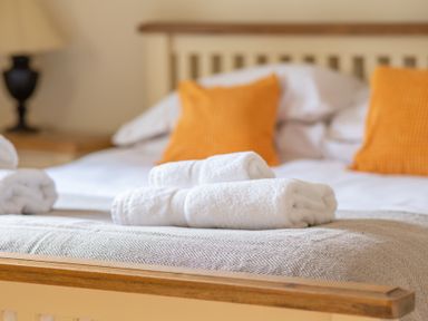 A bed with folded white towels on a blanket and orange pillows at Bull Pen in Graythwaite near Hawkshead