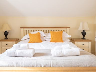 A bedroom with a double bed with orange pillows white towels on a blanket and bedside tables with lamps at Bull Pen in Graythwaite near Hawkshead
