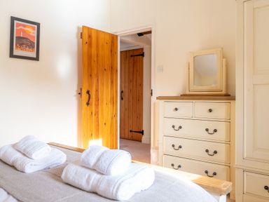 A bedroom with a bed topped with folded towels a wooden door and a cream dresser with a mirror at Bull Pen in Graythwaite near Hawkshead