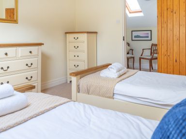 A bedroom with two single beds, a dresser, a chest of drawers, and two chairs in an adjoining room at Bull Pen Graythwaite near Hawkshead