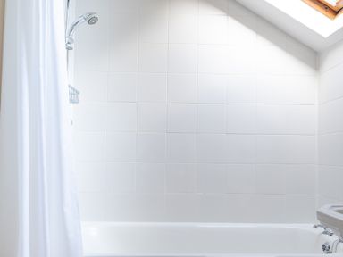A bathroom with a white bathtub showerhead curtain and skylight at Bull Pen Graythwaite near Hawkshead