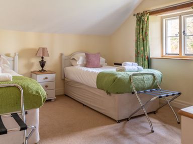 A bedroom with two single beds a bedside table and a window with green curtains at Bull Pen Graythwaite near Hawkshead