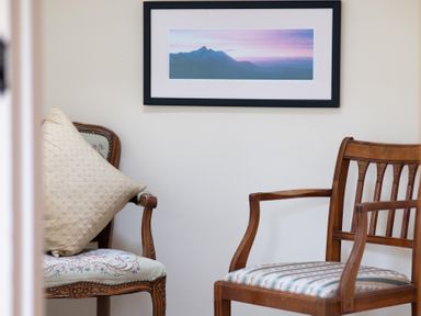Two wooden chairs with cushions and a framed picture of mountains on the wall at Bull Pen in Graythwaite near Hawkshead
