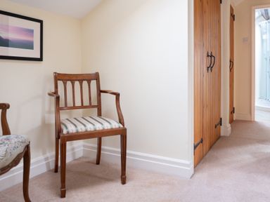 A hallway with two wooden chairs and wooden doors leading to a bathroom at Bull Pen Graythwaite near Hawkshead