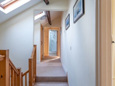 A hallway with stairs and wooden railing leading to a bathroom with a glass shower at Bull Pen in Graythwaite near Hawkshead