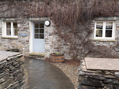 A stone cottage exterior with a gray door and two white framed windows at Bull Pen Graythwaite near Hawkshead