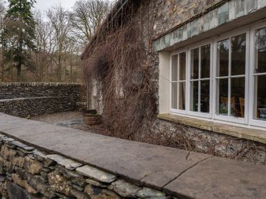 A stone wall and window of a stone building with bare vines outside at Bull Pen in Graythwaite near Hawkshead