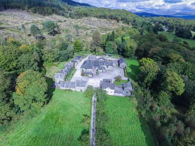 A group of stone buildings with slate roofs surrounded by green lawns and trees in a rural landscape