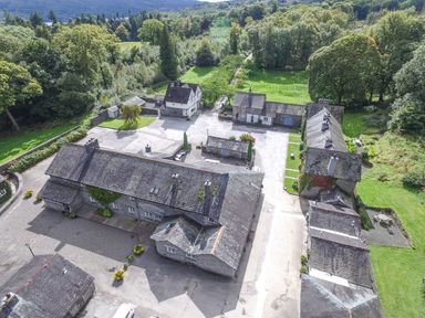 An aerial view of several stone buildings with slate roofs surrounded by trees and grass at Briar in Graythwaite near Hawkshead