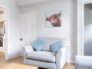 A grey armchair with two blue patterned cushions a painting of a cow on the wall and a wooden table in a living room at Briar in Graythwaite near Hawkshead