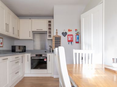 A kitchen with white cabinets a microwave oven and a wooden dining table with white chairs at Briar Graythwaite near Hawkshead