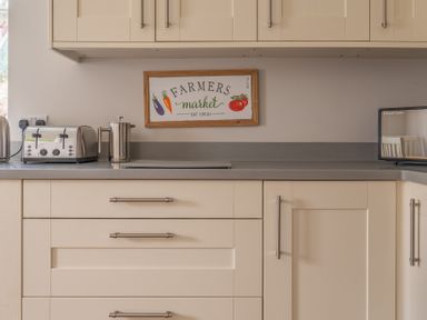 A kitchen counter with a toaster coffee press and microwave below wall cabinets and a farmers market sign at Briar in Graythwaite near Hawkshead