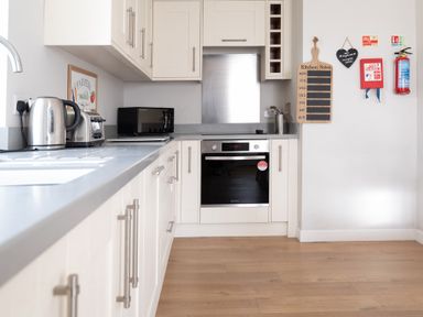 A kitchen with a kettle toaster and microwave on the counter an oven a kitchen notes board fire blanket and fire extinguisher on the wall at Briar Graythwaite near Hawkshead
