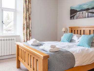 A bedroom with a wooden bed frame two blue pillows folded towels on the bed and floral curtains at Briar in Graythwaite near Hawkshead
