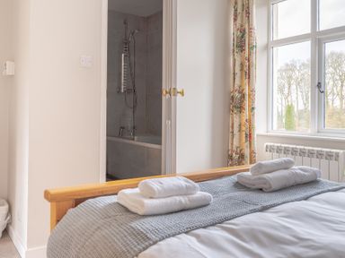 A bedroom with a wooden bed frame towels on the bed and an open door showing a bathroom with a bathtub at Briar in Graythwaite near Hawkshead
