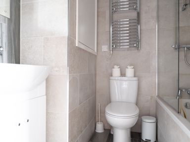 A bathroom with a toilet, toilet brush, towel heater, sink, bathtub, and waste bin at Briar Graythwaite near Hawkshead