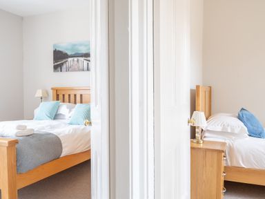 Two bedrooms separated by a white double door each with a wooden bed a bedside table and a lamp at Briar Graythwaite near Hawkshead