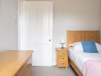 A bedroom with a wooden bed and nightstand with a lamp a blue pillow and a pink blanket at Briar in Graythwaite near Hawkshead