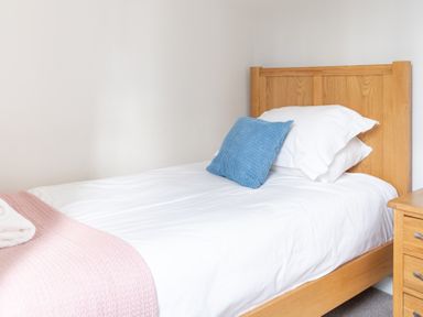A single wooden bed with white bedding and a blue cushion beside a wooden bedside table at Briar in Graythwaite near Hawkshead