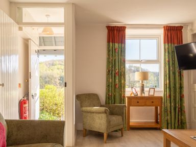 A sitting area with armchairs and a wooden table under a window with floral curtains at Eel House Cottage Graythwaite Estate near Hawkshead