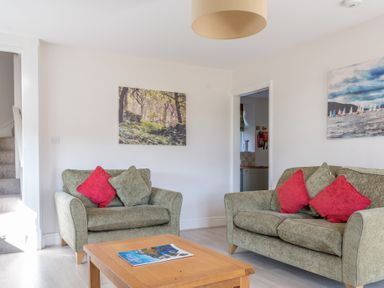 A living room with two green sofas with red and green cushions a wooden coffee table and paintings on the walls at Eel House Cottage in Graythwaite Estate near Hawkshead