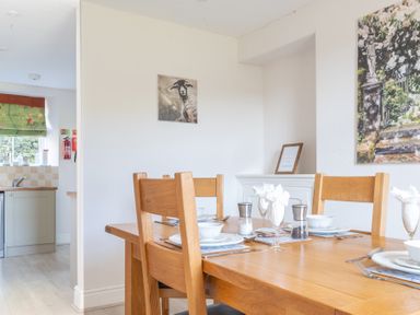 A dining area with a wooden table set for four with bowls plates and napkins near a kitchen with a sink at Eel House Cottage Graythwaite Estate near Hawkshead