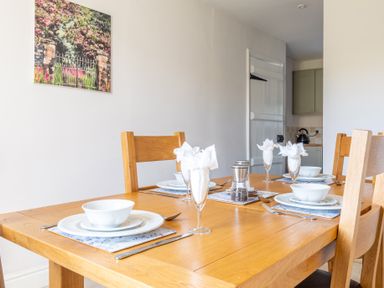 A dining table set with white bowls plates and folded napkins in glasses at Eel House Cottage Graythwaite Estate near Hawkshead