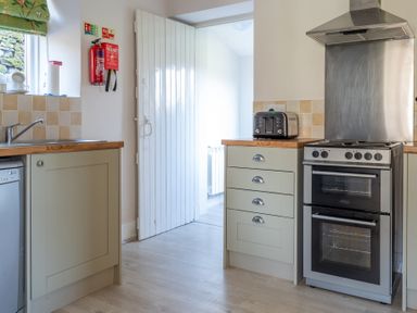 A kitchen with a stove oven unit a toaster a sink and an open door at Eel House Cottage Graythwaite Estate near Hawkshead