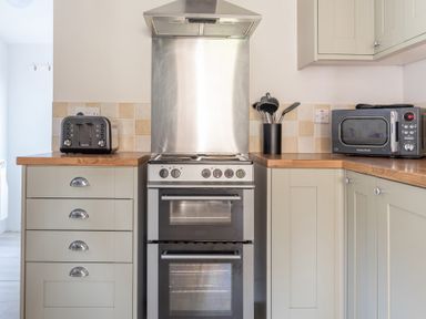 A kitchen with a stove and oven between cabinets with a toaster on the left and a microwave with kitchen utensils on the right at Eel House Cottage Graythwaite Estate near Hawkshead