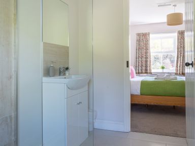 A bathroom sink with a mirror and soap dispenser next to a bedroom with a bed and window at Eel House Cottage in Graythwaite Estate near Hawkshead