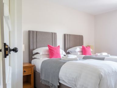 A bedroom with two single beds with grey headboards and pink pillows at Eel House Cottage Graythwaite Estate near Hawkshead