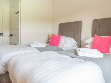 A bedroom with two single beds white linens gray throws and pink pillows at Eel House Cottage in Graythwaite Estate near Hawkshead