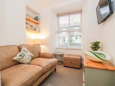 A living room with a brown sofa a small table an ottoman a wall-mounted television and a cabinet with a plant and decorative bowl at Pottergill in Windermere