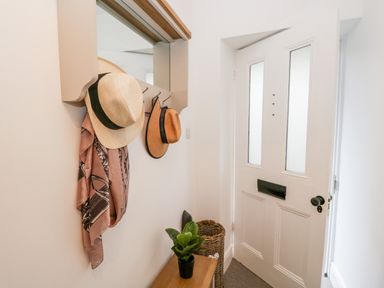 An entryway with a white front door a coat rack with hats and a scarf a small wooden bench with a potted plant and a woven basket next to the door at Pottergill in Windermere
