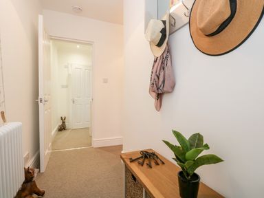 A hallway with a wooden bench holding a plant and keys two hats and a scarf hanging on hooks and an open door showing another hallway with a rabbit figurine at Pottergill in Windermere