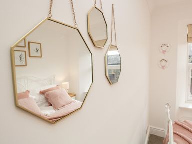 Three hanging mirrors reflecting a bed with pink pillows and a bedside table in a bedroom at Pottergill in Windermere