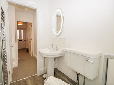 A bathroom with a white pedestal sink and oval mirror next to a white toilet with a silver flush handle at Pottergill in Windermere