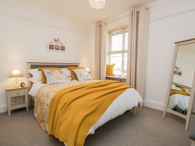 A bedroom with a bed with yellow and floral bedding two bedside tables with lamps a window with curtains and a mirror at Pottergill Windermere