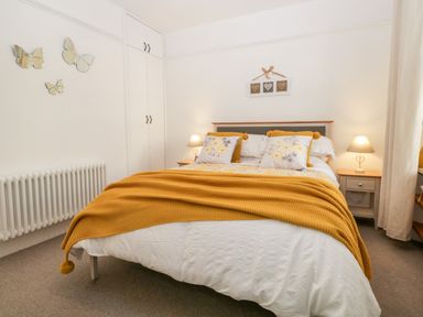 A bedroom with a double bed covered with white bedding and a yellow throw with matching cushions bedside tables with lamps built-in wardrobes and butterfly wall decor at Pottergill in Windermere