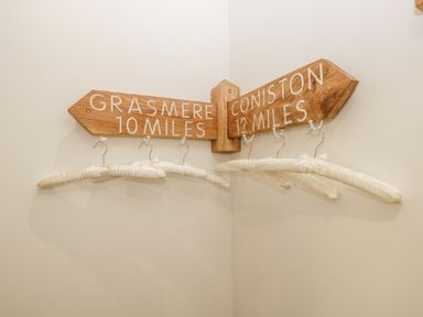 Wooden signpost with distances to Grasmere and Coniston with padded hangers hanging below on a wall at Pottergill in Windermere