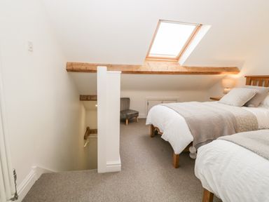 A bedroom with two beds, a skylight window, a chair, and a lamp at Pottergill in Windermere