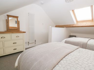 A bedroom with two beds a dresser with a mirror a radiator and a skylight window at Pottergill in Windermere