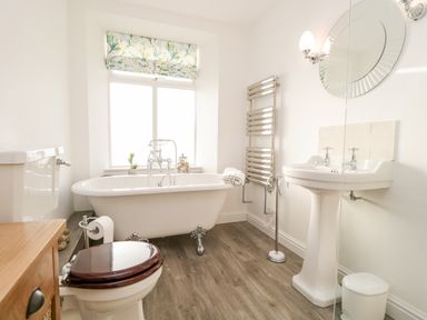 A bathroom with a clawfoot bathtub next to a window a pedestal sink a toilet with a wooden seat and a towel warmer at Pottergill in Windermere
