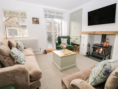 A living room with beige sofas green armchair wooden coffee table fireplace and wall mounted tv at Pottergill in Windermere