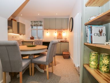 A dining area with a round table and four chairs next to an open kitchen with cabinets and hanging lights at Pottergill in Windermere