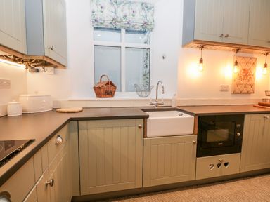 A kitchen with beige cabinets a white farmhouse sink under a window with floral blinds at Pottergill in Windermere