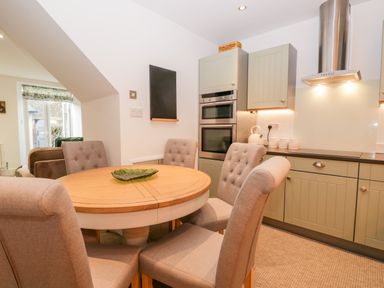 A kitchen with a round wooden table and upholstered chairs next to light green cabinets and stainless steel appliances at Pottergill in Windermere