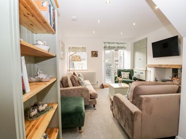 A living room with beige sofas a green armchair and a wooden bookshelf at Pottergill in Windermere
