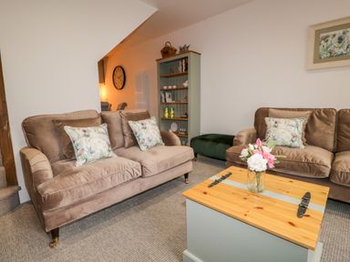 A living room with two brown sofas with floral cushions a wooden coffee table with flowers a green ottoman and a bookshelf at Pottergill in Windermere