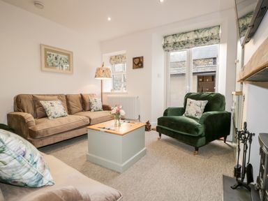 A living room with brown sofa green armchair floral cushions and a wooden coffee table at Pottergill in Windermere